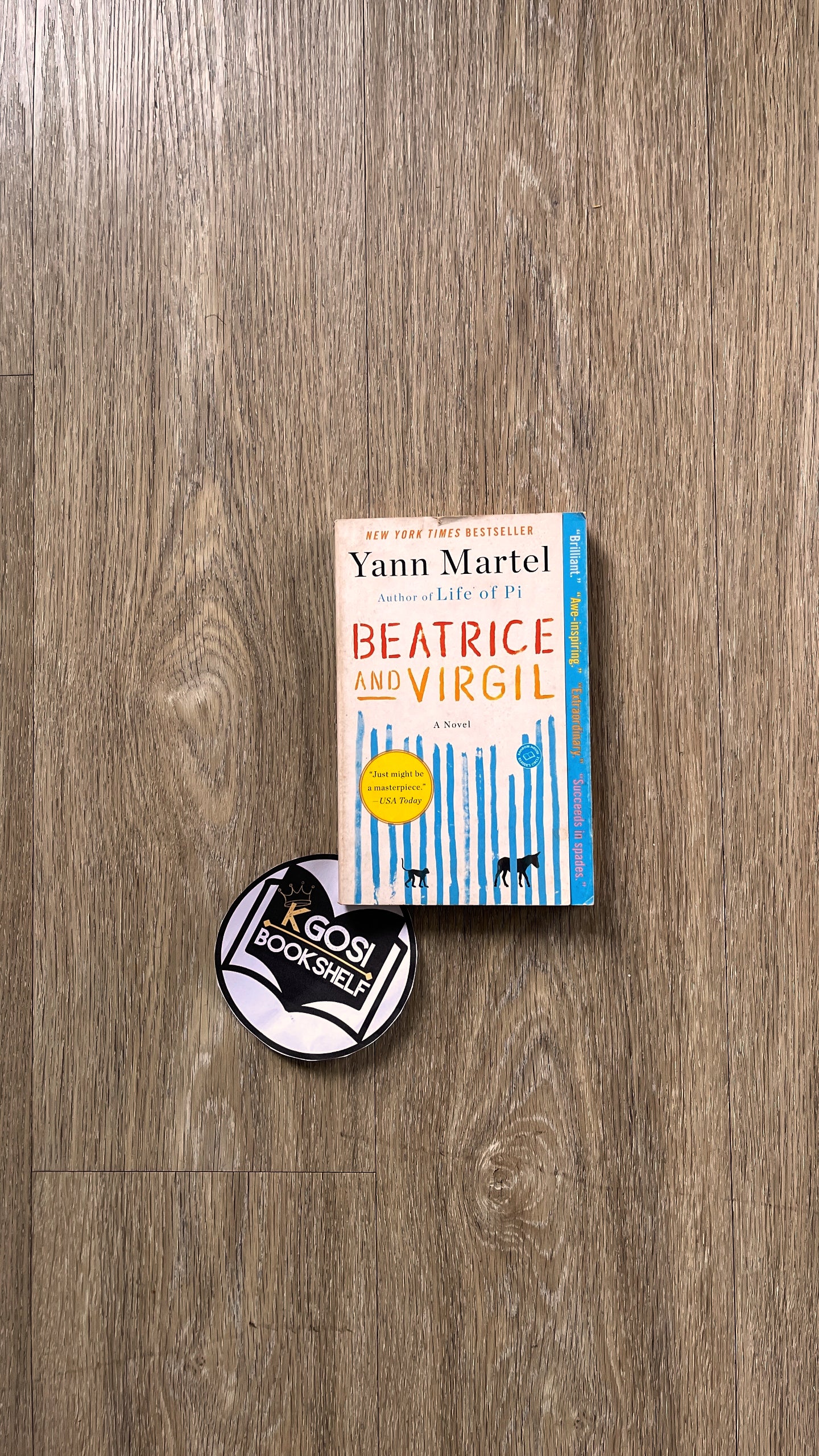 Book titled 'Beatrice and Virgil' by Yann Martel on a wooden surface with a sticker below.