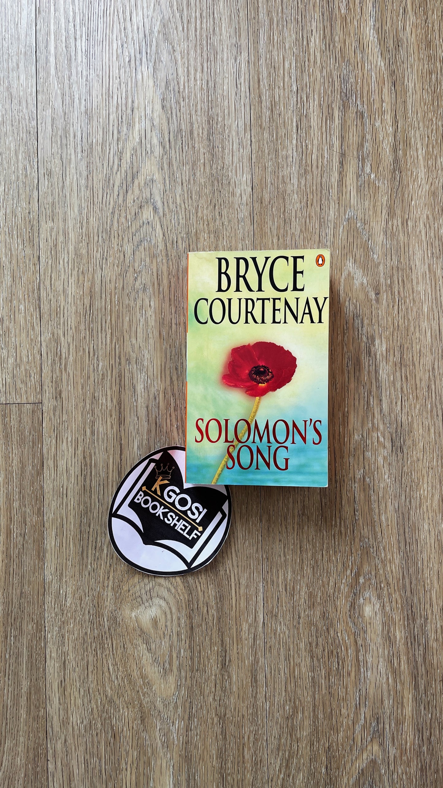 Book titled 'Solomon's Song' by Bryce Courtenay on a wooden surface with a badge.