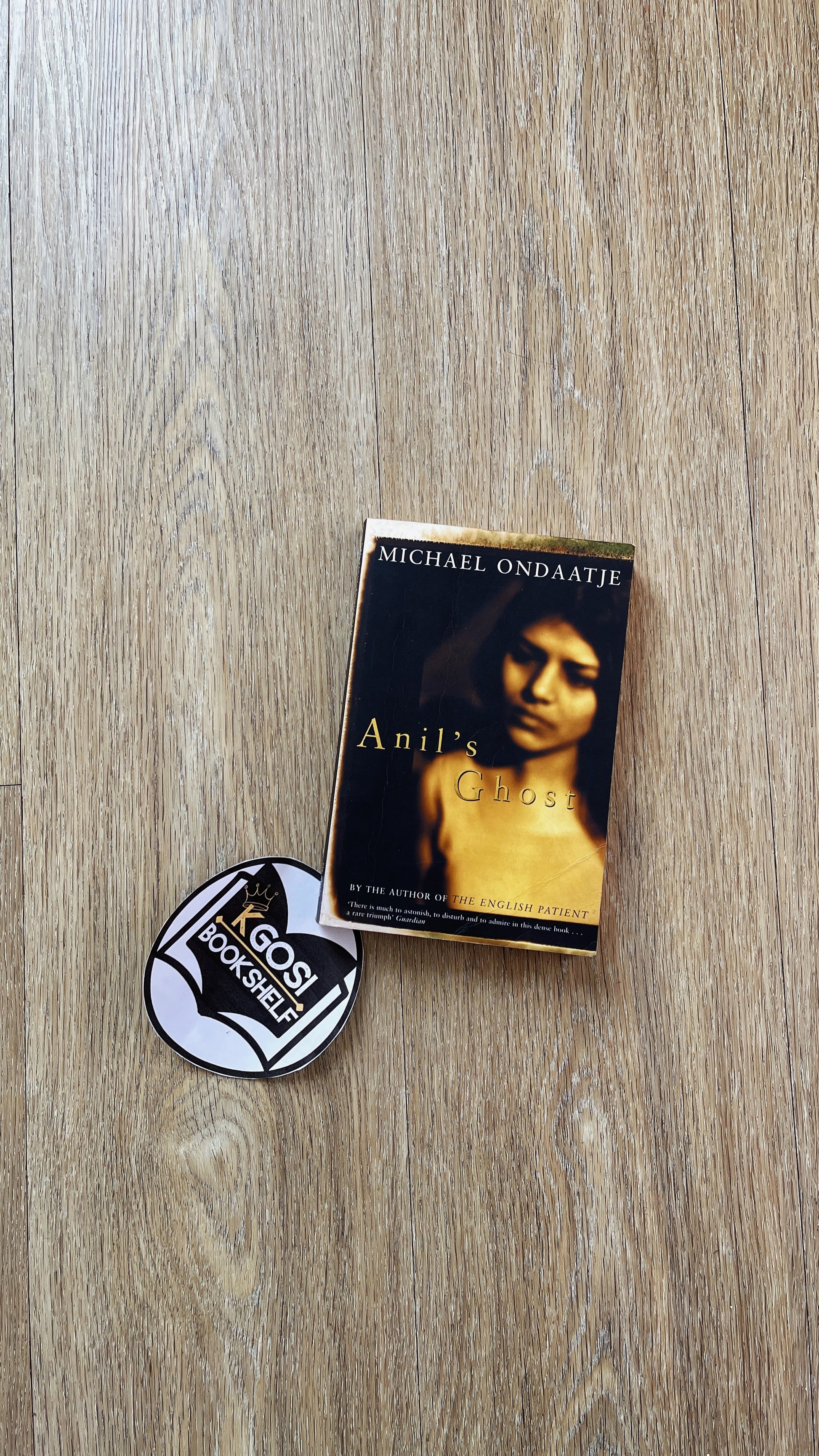 Book titled 'Anil's Child' by Michael Ondaatje with a button on a wooden surface