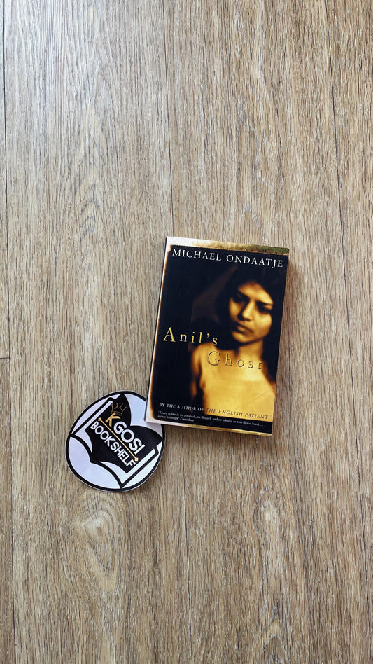 Book titled 'Anil's Child' by Michael Ondaatje with a button on a wooden surface