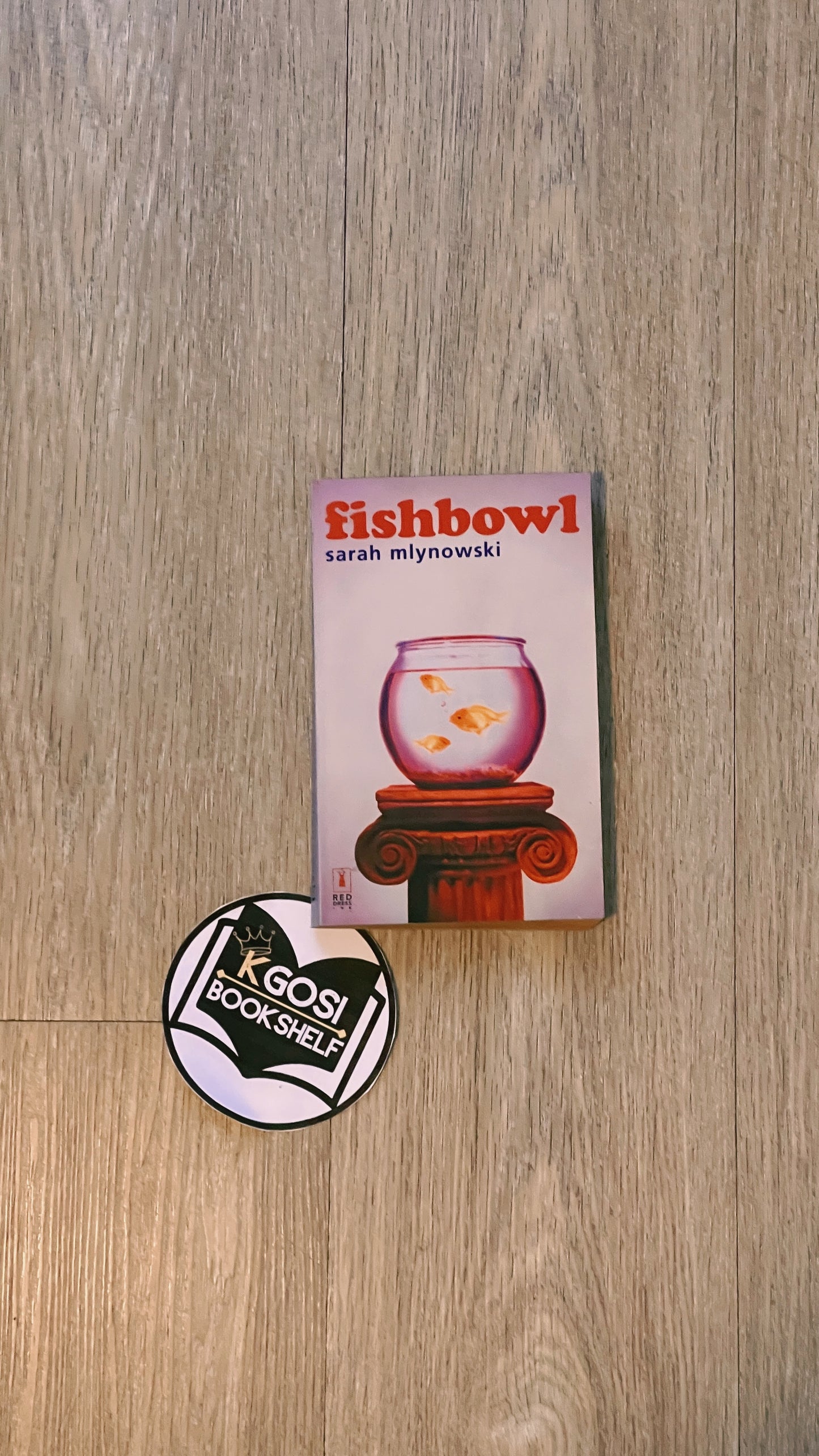 Book titled 'fishbowl' by Sarah Mlynowski on a wooden surface with a Kagosi Booksshelf sticker.